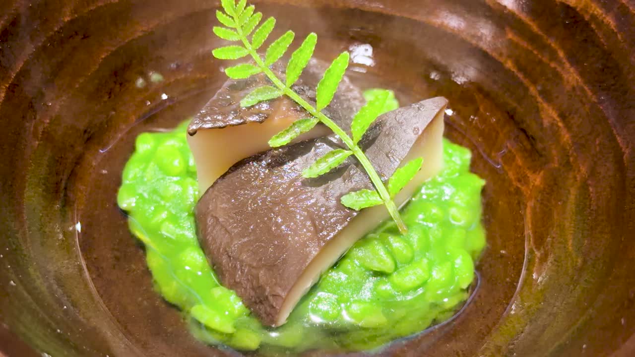 Primo piano dall'alto di un piatto omakase giapponese fumante con funghi e una purea verde vivace.