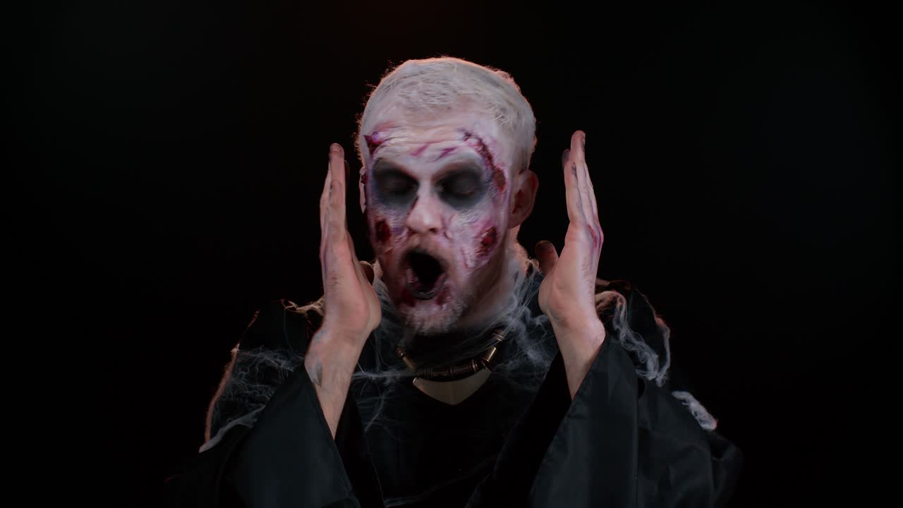 hombre aterrador halloween zombie levantando las manos en sorpresa mirando conmocionado por la victoria repentina