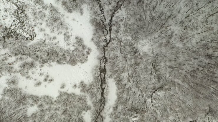 River stream flows in snow covered winter forest, aerial overhead