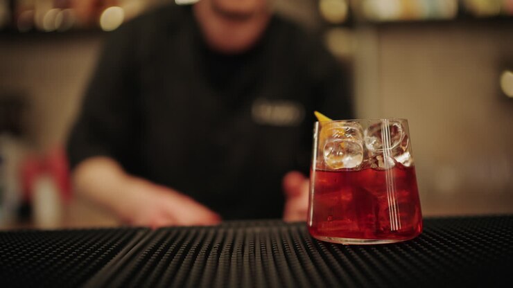 Primo piano di mani che spremono limone fresco in un bicchiere da cocktail con ghiaccio