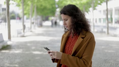 Serious-young-woman-using-smartphone-outdoor