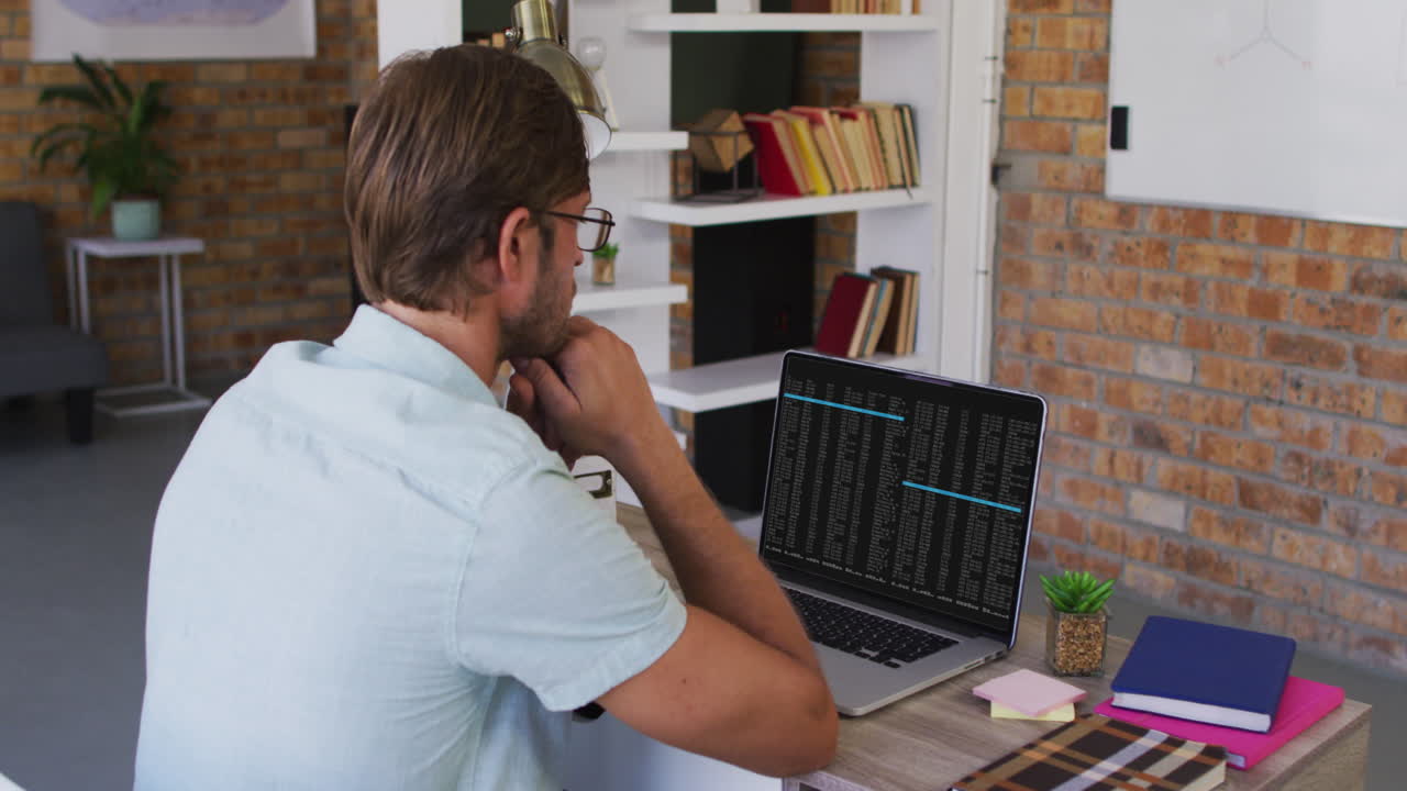Caucasian man sitting at desk watching coding data processing on laptop screen