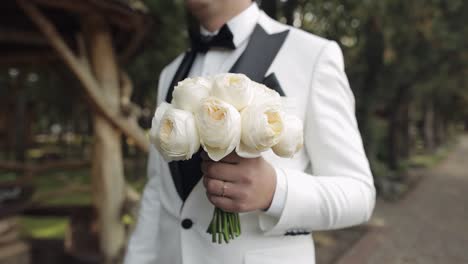 groom in a white suit holding a bouquet of white roses