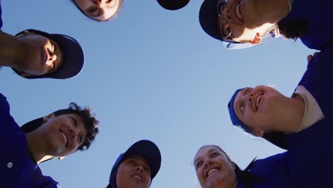 low angle view of diverse group of female baseball players in a huddle against blue sky