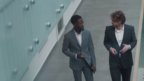 two male colleagues going along office hall and talking