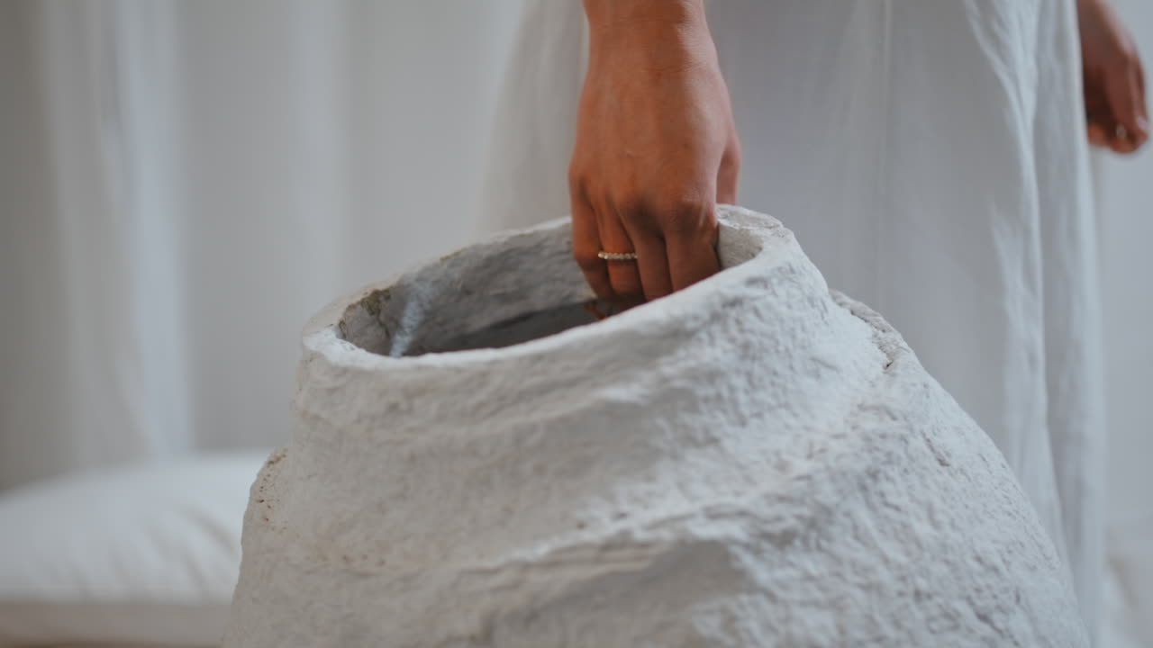 손가락은 손으로 만든 꽃병을 가까이 잡고 있습니다. 최소한의 페이퍼 마체 항아리를 가진 여성 예술가