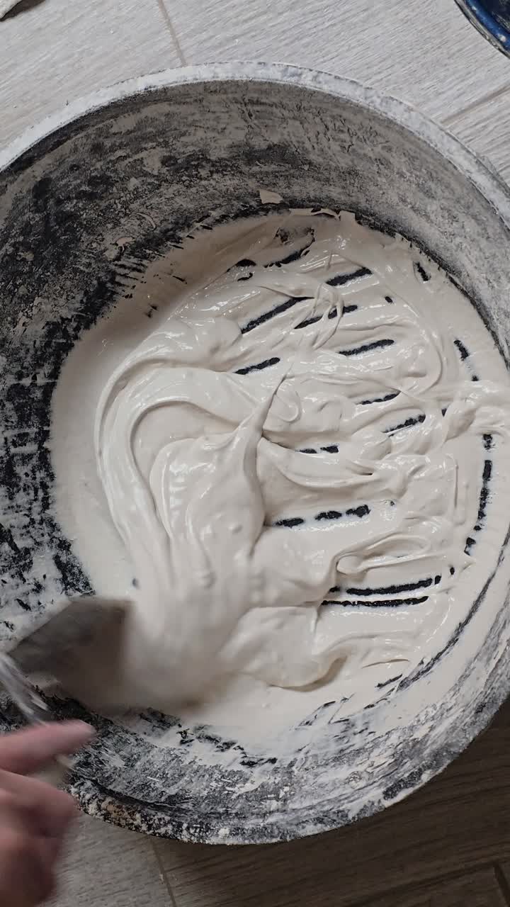 Male hand mixing white plaster with a spatula in a bucket during home renovation work