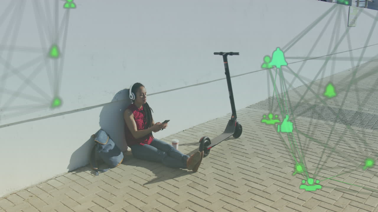 Two globes of digital icons against african american woman using smartphone sitting on the street