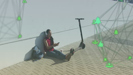 two globes of digital icons against african american woman using smartphone sitting on the street