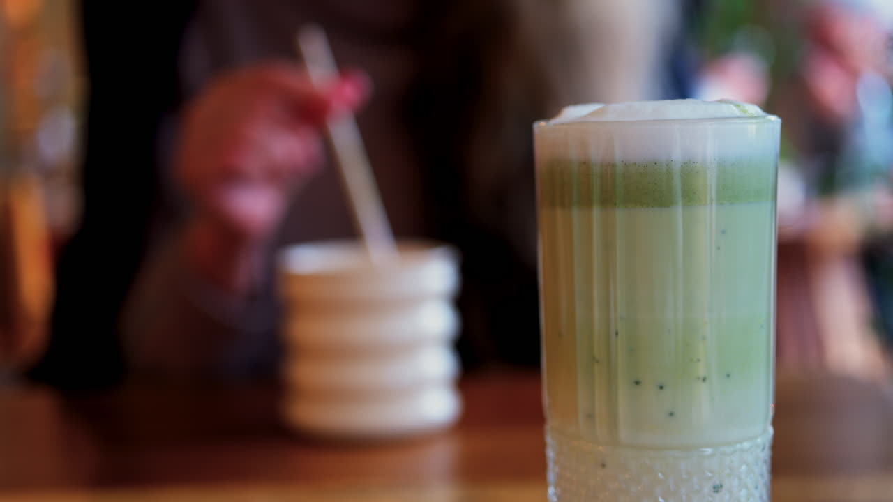 Close de um matcha latte com uma mulher bebendo em uma mesa em um café no plano de fundo