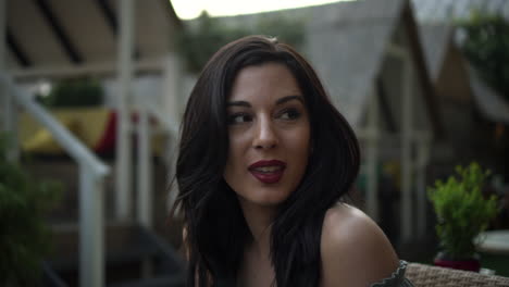 slow motion portrait of a beautiful hispanic latino young woman looking at the camera and show emotions from serious to smiling and laughing while seated in a club at sunset