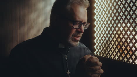 priest saying prayer of absolution in confessional booth