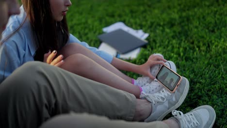 a young couple sitting on the grass, talking on the phone