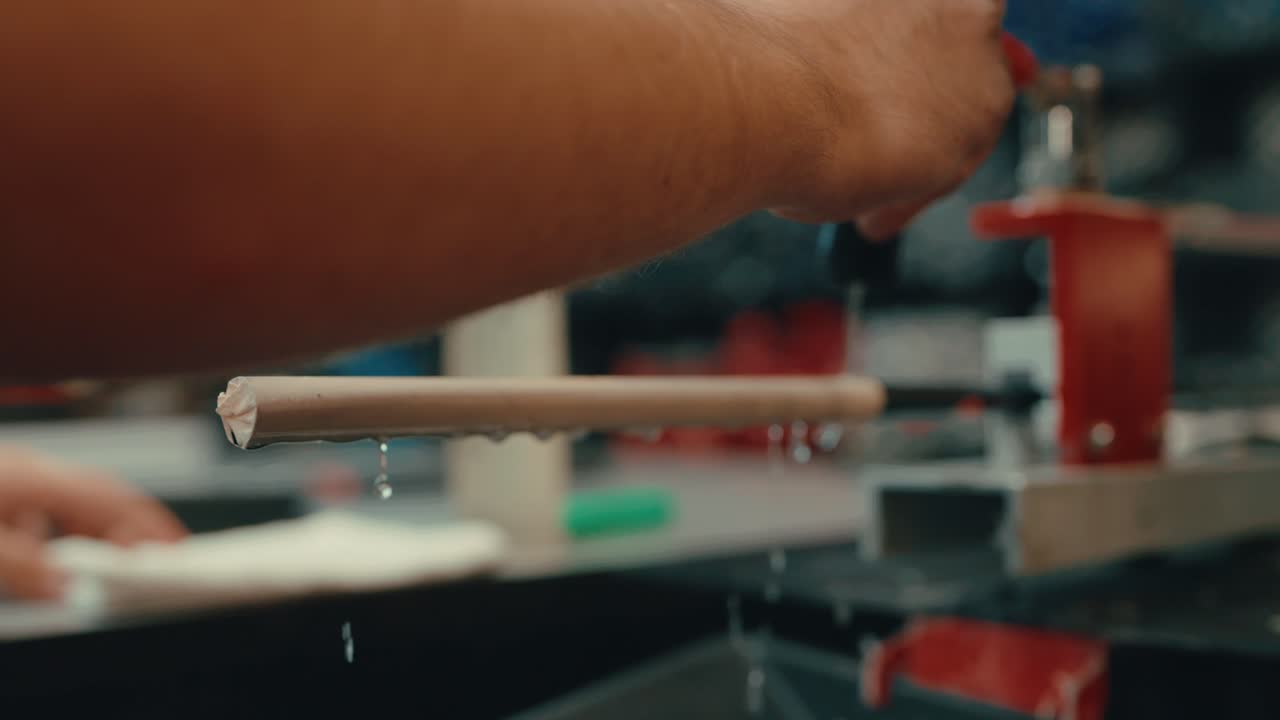 Water droplets dripping down golf club shaft as male builder's hands squeeze water onto grip to prepare for custom fit golf club wedge build in workshop in slow motion