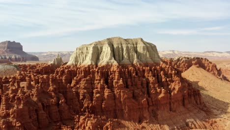 Gorgeous-rising-aerial-drone-shot-of-the-beautiful-Goblin-Valley-Utah-State-Park-with-pointy-red-hoodoo-rock-formations-and-red-and-white-Butte's-looming-above-on-a-warm-sunny-summer-day