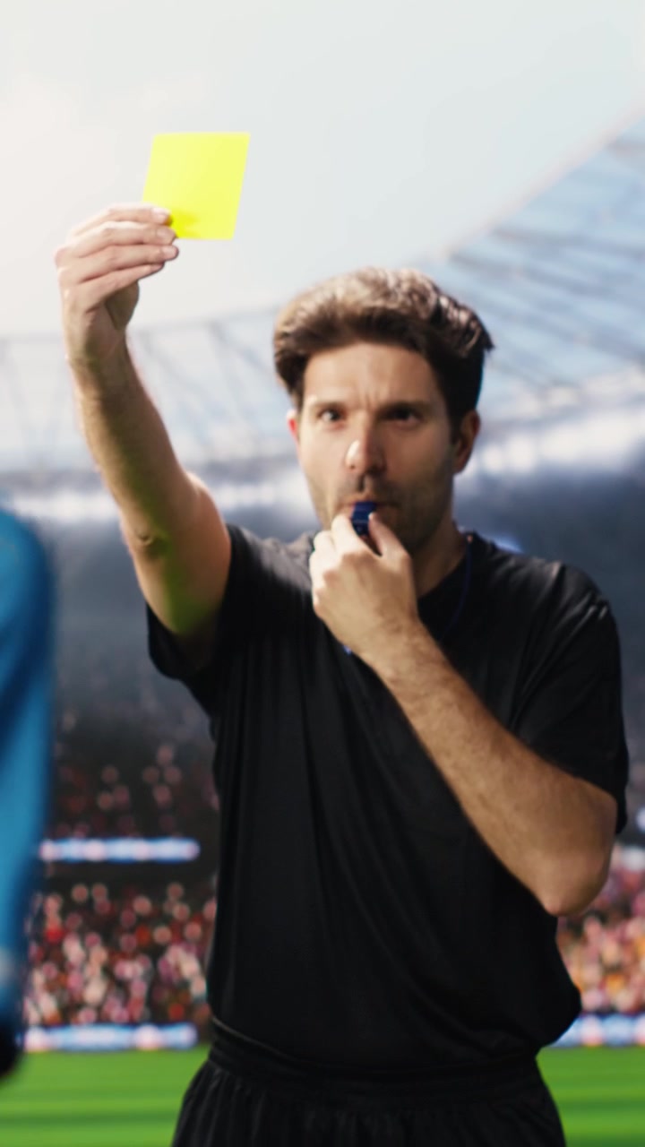 Video verticale: Arbitro di calcio mostra un cartellino giallo a un giocatore dopo aver commesso un fallo.