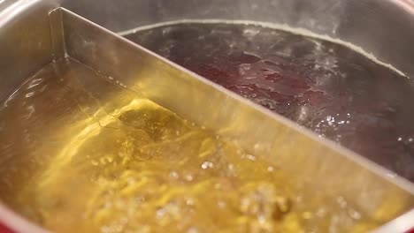 close-up of two types of broth boiling in a divided stainless steel pot, showcasing simmering liquid and steam.