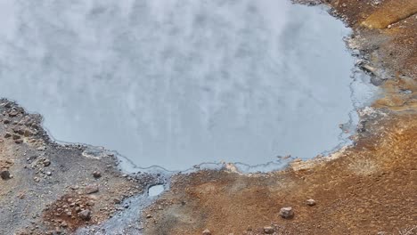 an aerial drone's fixed view of the muddy border with steam at engjahver's steam lake on the reykjanes peninsula in iceland