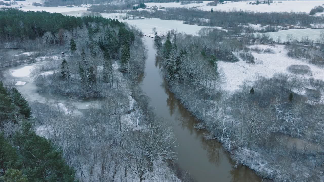 Veduta aerea panoramica della valle del fiume Abava in una giornata invernale nuvolosa, campi coperti di neve, il fiume Abava con acque scure di piena, ampia ripresa con drone che avanza, inclinazione verso il basso