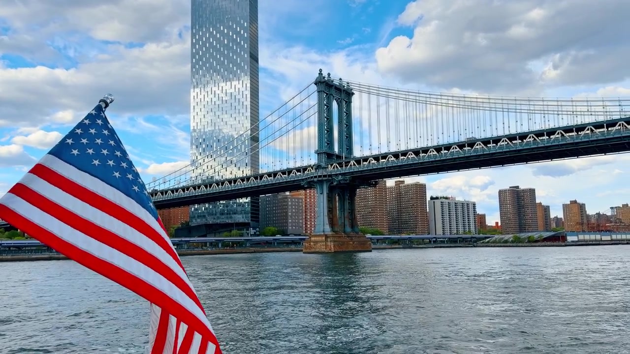Bandiera americana che sventola su una barca vicino al Ponte di Manhattan a New York. Primo piano sulla bandiera degli Stati Uniti su un'imbarcazione con il Ponte di Manhattan e gli edifici della città dall'altra parte dell'East River