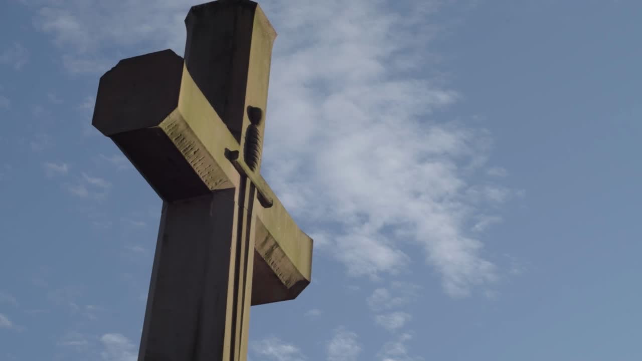Large stone carved cross against blue sky and clouds wide panning shot