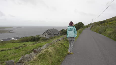 tracking shot of girl walking on a sky road looking at atlantic ocean and the coast of ireland in 4k