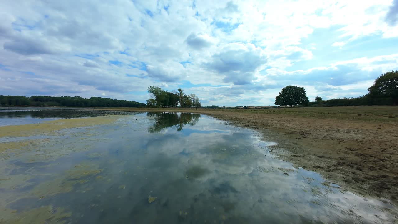 Cinematic FPV drone view gliding over tranquil water and wetland habitat with birds and reflections, Eye Brook, UK