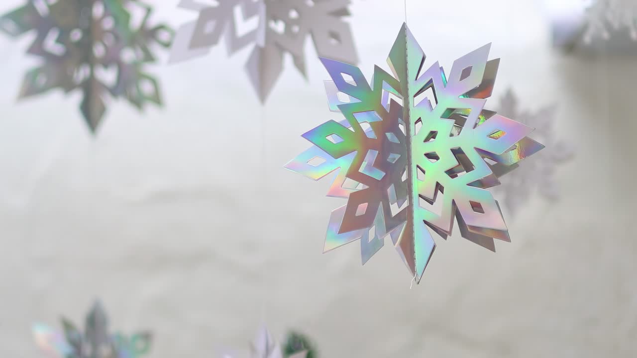 Close-up view of shimmering holographic snowflakes twirling softly against a neutral background.