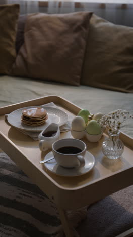 breakfast tray with pancakes, coffee, and easter eggs on sofa