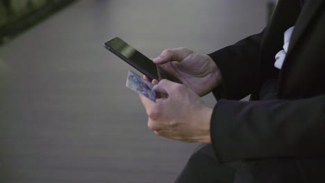 young male hands putting bank card data on phone, paying online