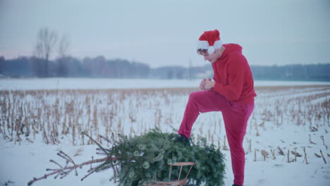 man rubbing hands with christmas tree on snow covered landscape against sky