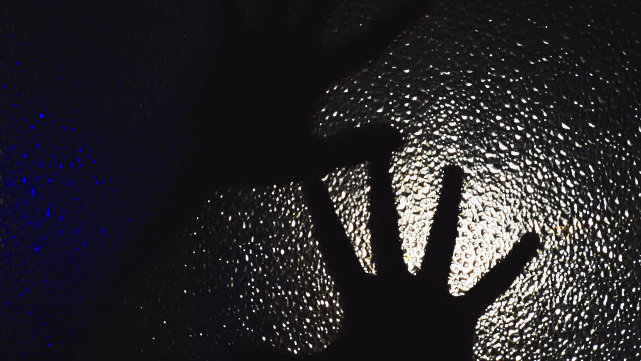 la mano helada de un hombre poseído se arrastra y se arrastra por el vidrio en la oscuridad bajo la luz parpadeante, enviando escalofríos por la columna vertebral