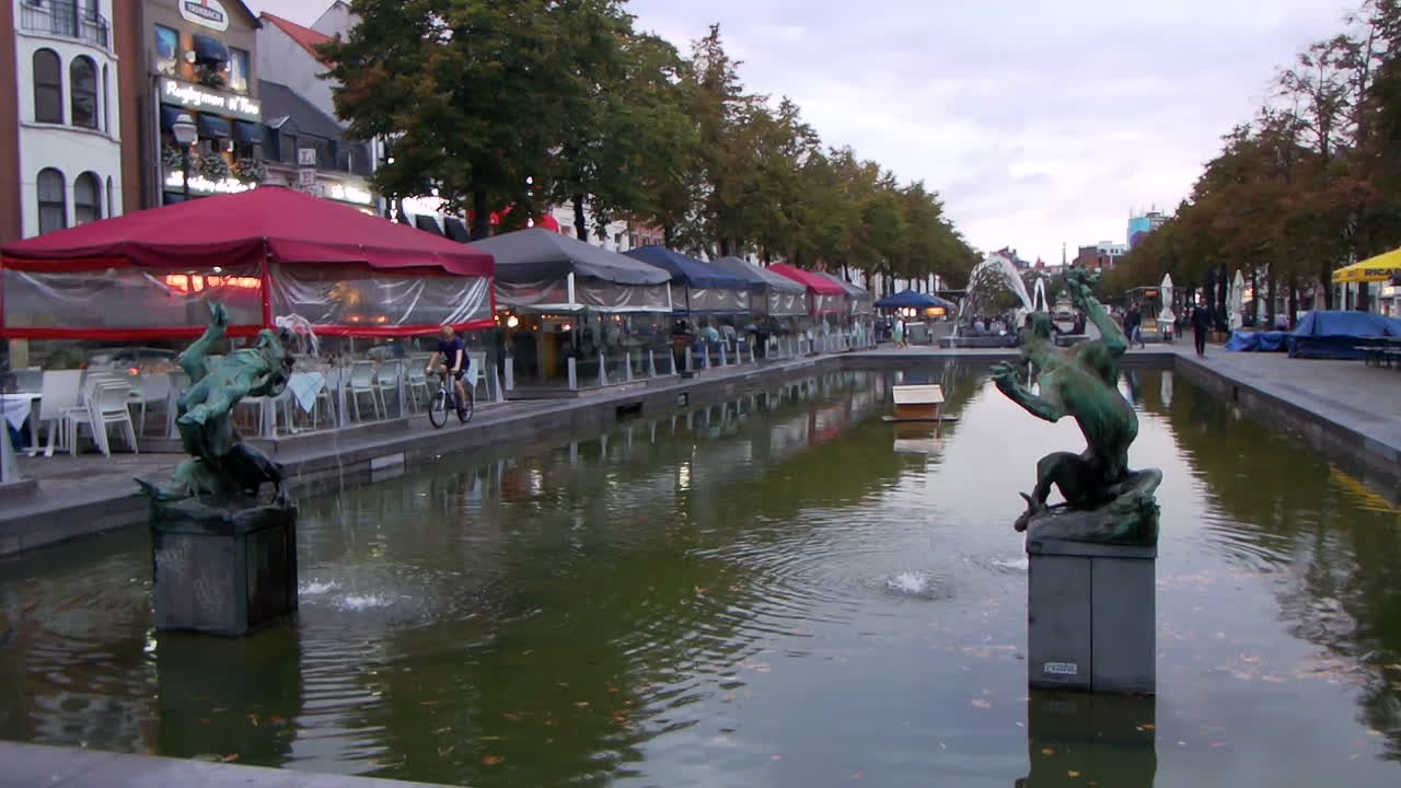 Outdoor canal with sculptures, trees, and cafés along the water in a lively Brussels city scene