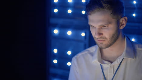 Face-portrait-of-man-working-in-server-room-with-laptop.-technician-doing-a-checkup-in-the-server-room.-Caucasian-engineer-wearing-grey-worker-jacket