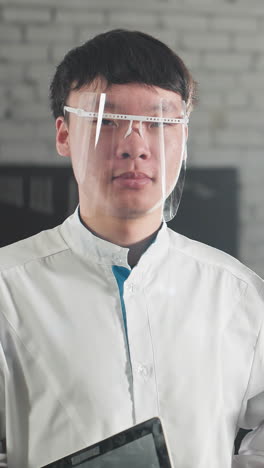 남성 기술자는 태블릿을 들고 따뜻한 미소로 고개를 끄덕이고, 그의 동료는 부드러운 미소로 안경을 조정합니다. 둘 다 실험실 코트를 입고 자동차 워크 환경에서 자신감 있게 서 있습니다.