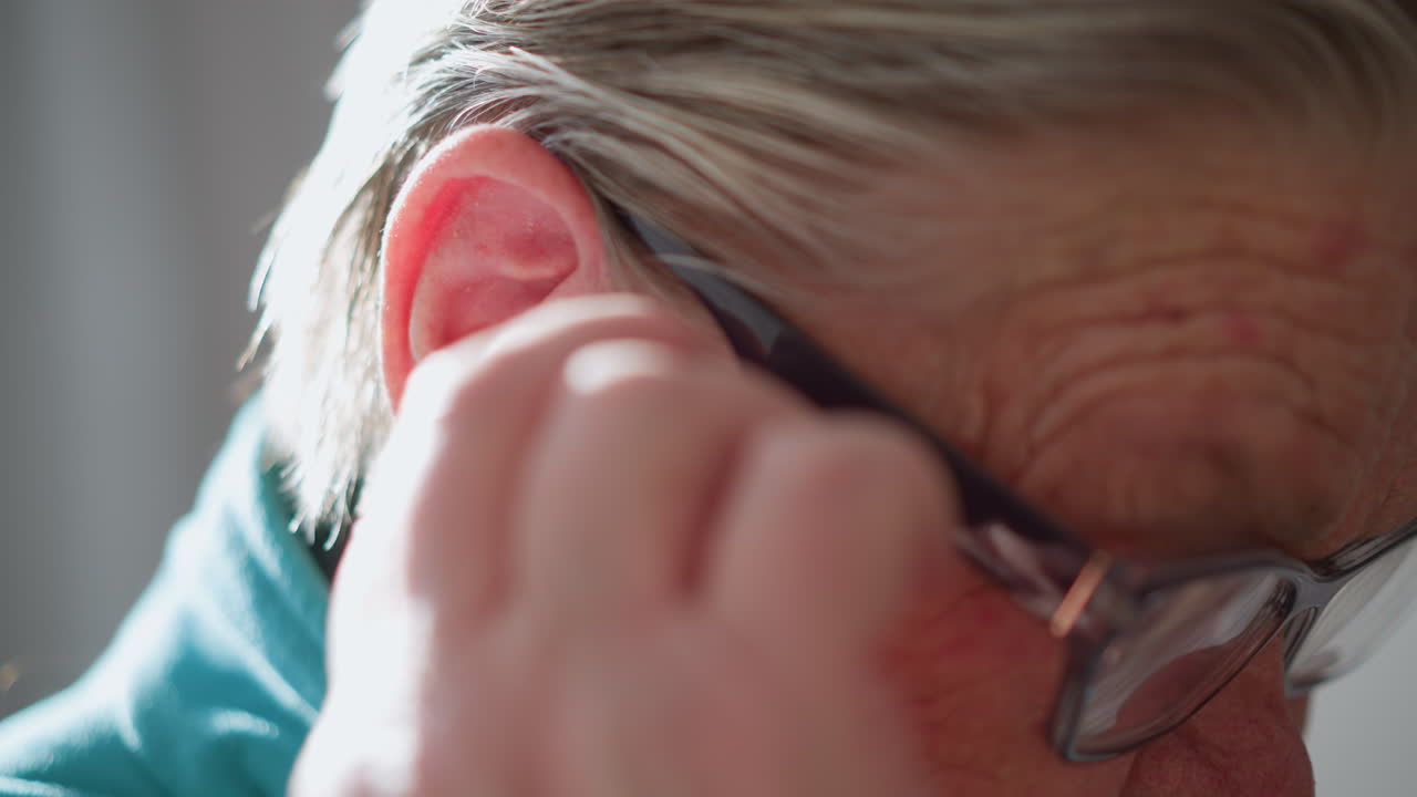 Elderly woman adjusting glasses while reading book with magnifying glass. Soft indoor lighting highlights focused expression, hands delicately handling glasses, eyes narrowing as she reads with care