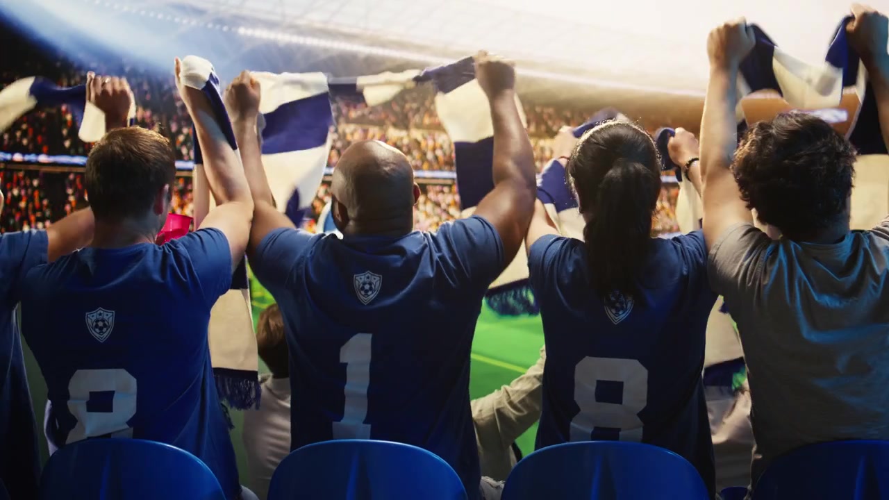 Primer plano de aficionados al fútbol felices levantando bufandas en un estadio abarrotado.