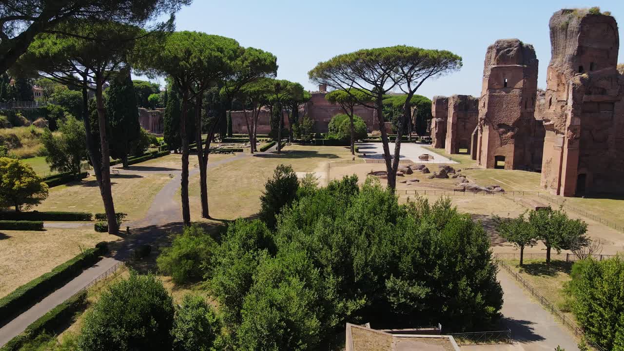 Drone glides between trees toward grand Roman ruins in Caracalla thermal site