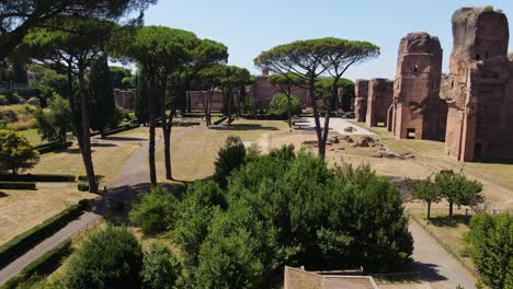 drone glides between trees toward grand roman ruins in caracalla thermal site