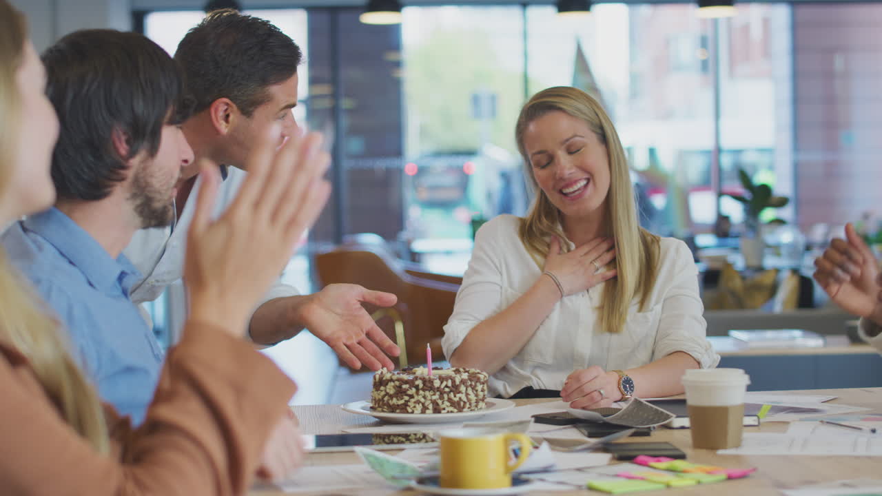 Colleagues Celebrating Businesswoman's Birthday At Meeting Around Table In Modern Open Plan Office