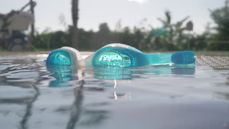 a closeup of blue goggles on an open pool surface on a sunny day