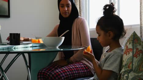 Young-mother-using-laptop-while-her-daughter-is-eating-fruits-at-home-4k