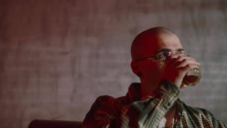 young man drinking a drink in a room with red lighting