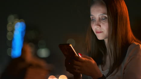 young woman tourist travels through the night megalopolis and writes text messages on social networks about the journey holds the phone in her hands and looks at the screen of the gadget