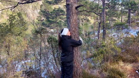Woman-embracing,-hugging-and-showing-love-to-a-pine-tree-out-in-nature---Sunny-winter-day-static