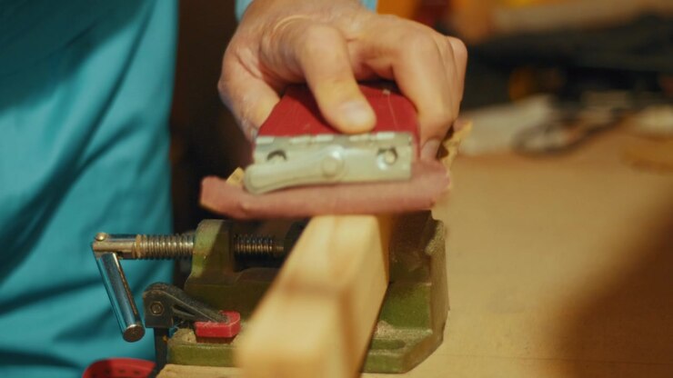 Close-up of a hand using a red sanding block to smooth a wooden plank clamped in a vise. Authentic DIY woodworking footage for craft, carpentry and maker projects