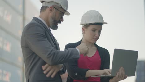 propietario de negocios logísticos, ejecutivo y secretario o asistente, comprobar la carga de carga y el proceso de envío en tiempo real o el progreso del plan de inversión más en el portátil en el patio de contenedores comerciales.