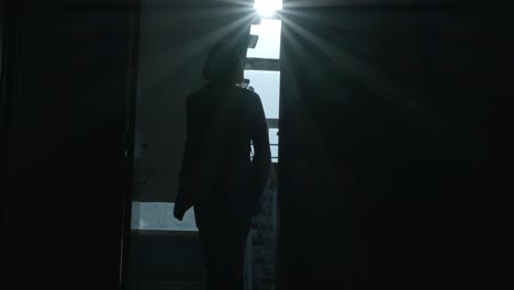 man walks along a dark long corridor. abandoned building, dark corridor, dark silhouette of a man, light in the doorway, ruins, broken windows, rust, unfinished