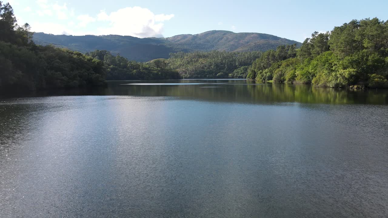 A calm river surrounded by lush green forests and hills, reflecting the blue sky and clouds. A peaceful, untouched natural setting ideal for nature and outdoor-themed footage. Cortegada, Galicia.