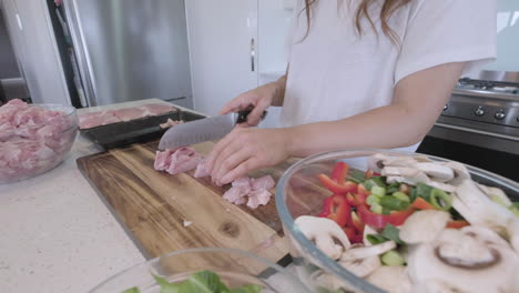 Side-on-wide-angle-sliding-shot-of-woman-preparing-chicken-and-vegetables-for-asian-stir-fry